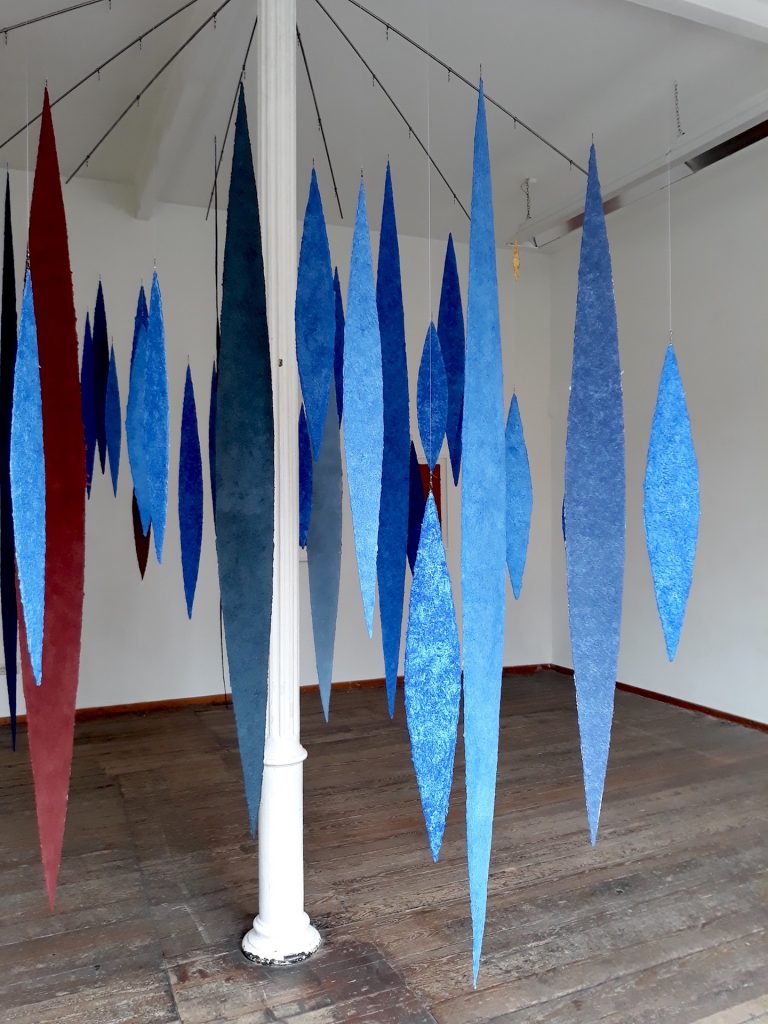 An der Ausstellung papier = kunst 9 im NKV Aschaffenburg im KunstLANDing nimmt Helmut Dirnaichner mit einer Raumarbeit aus 48 geschöpften, schwebenden Lanzettformen aus Lapislazuli und Zinnober teil.